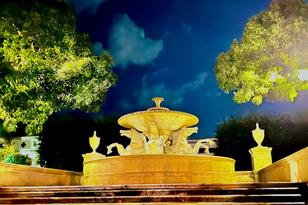Illuminated ornate fountain at night with dramatic blue sky and trees